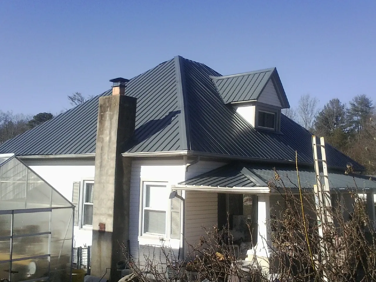 Dark blue standing seam metal roof on a white farmhouse with dormer — Slate & Tile Roof Repair by Roofing Brothers in Gustine