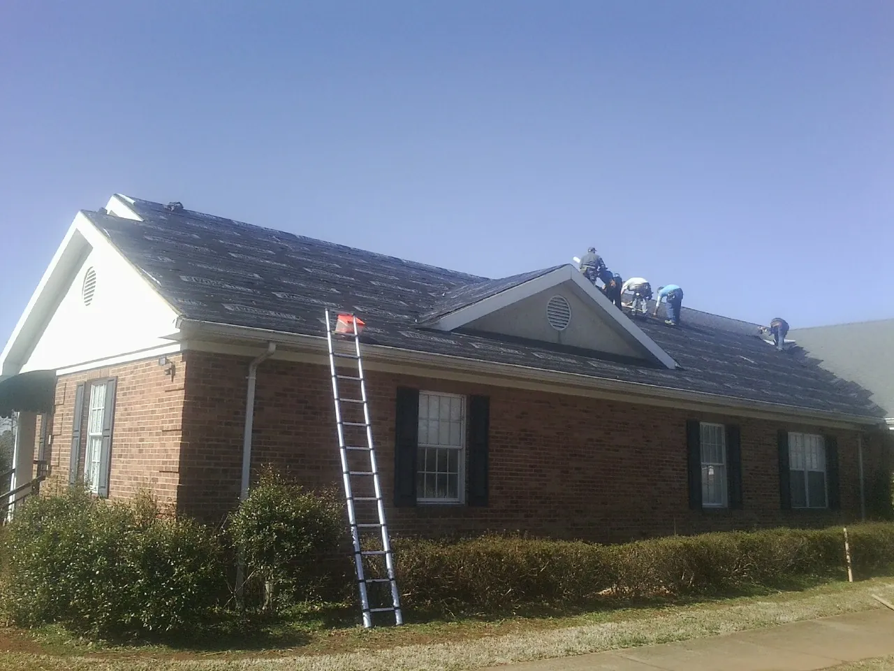 Crew tearing shingles off a brick ranch roof with a ladder set — Metal Roof Repair work by our crew in Gustine