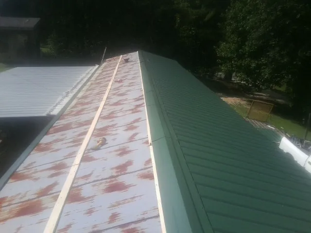 Old rusted panels beside newly installed green metal roofing — Wind Damage Roof Repair by Roofing Brothers in Gustine