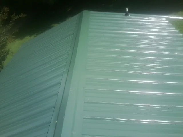 New green metal panels meeting at the ridge of a roof — Flat Roof Repair work by our crew in Gustine