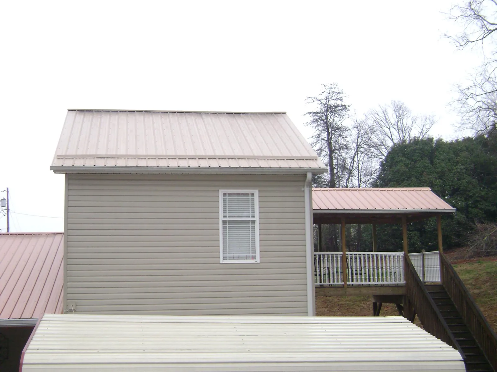 Tan metal roofs on a two story addition and attached porch, from a Roof Replacement job in Gustine